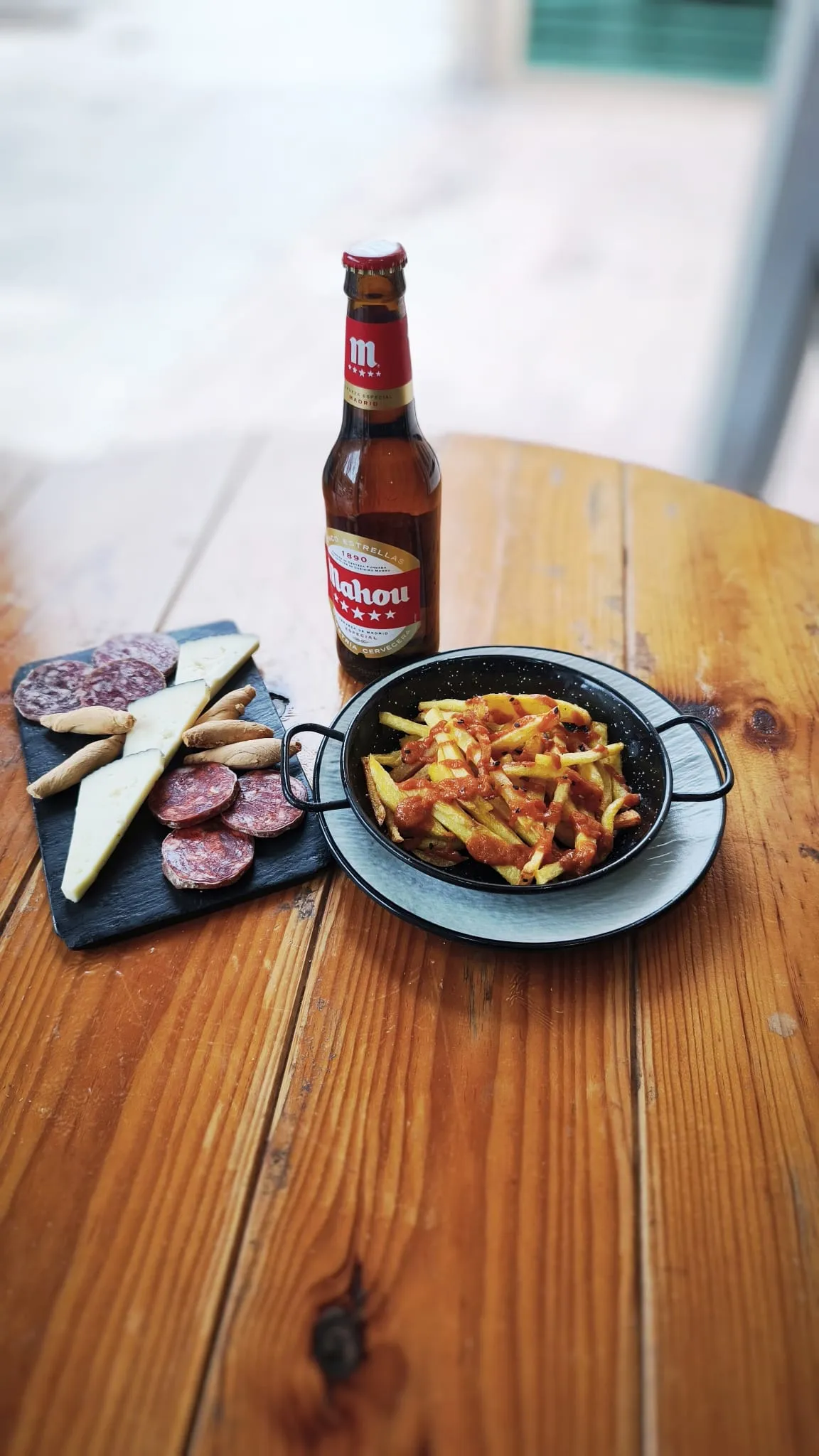 Patatas con salsa, tabla de queso y embutido y un botellín de Mahou